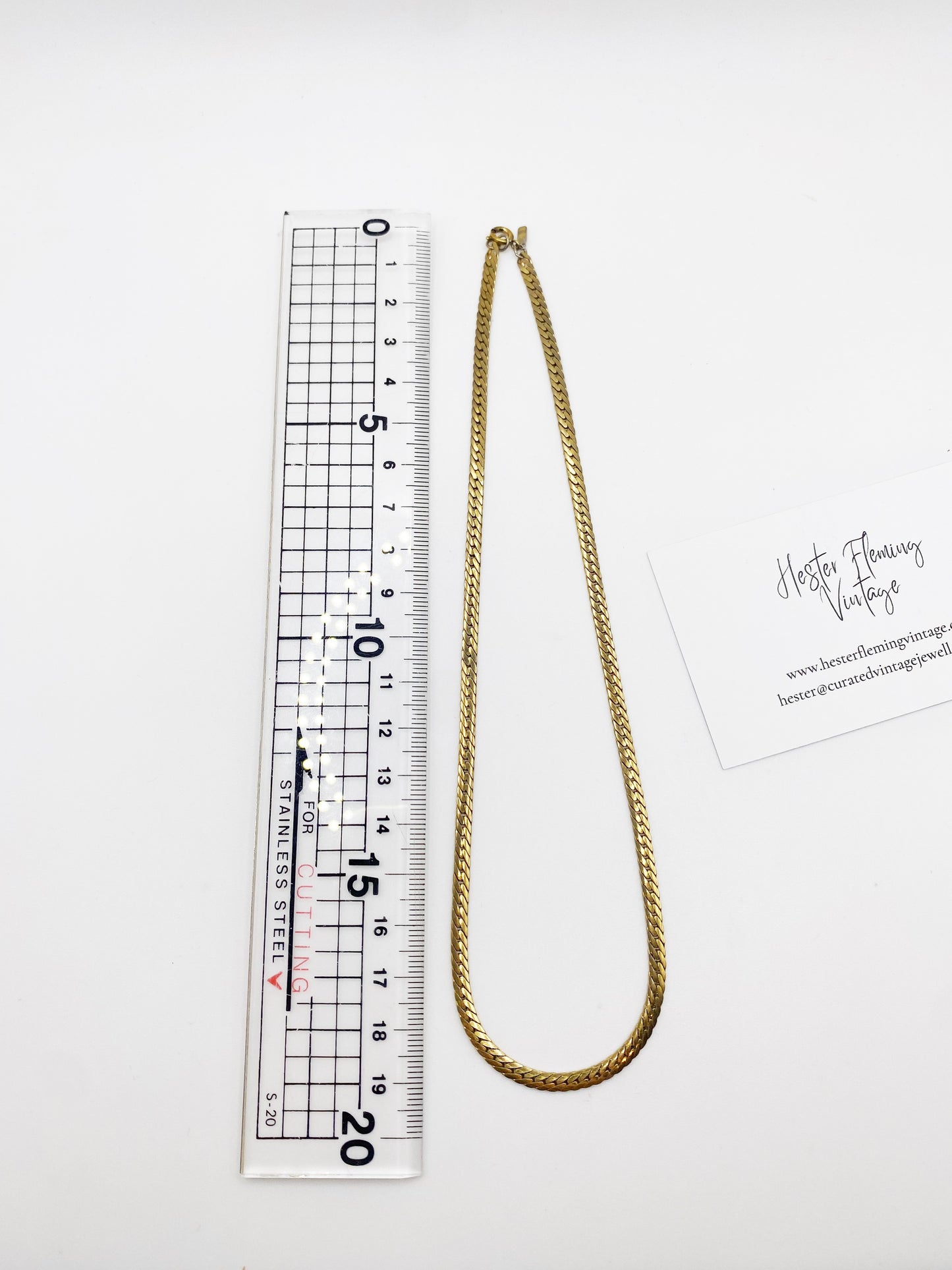 Gold chain necklace next to a ruler on a white background