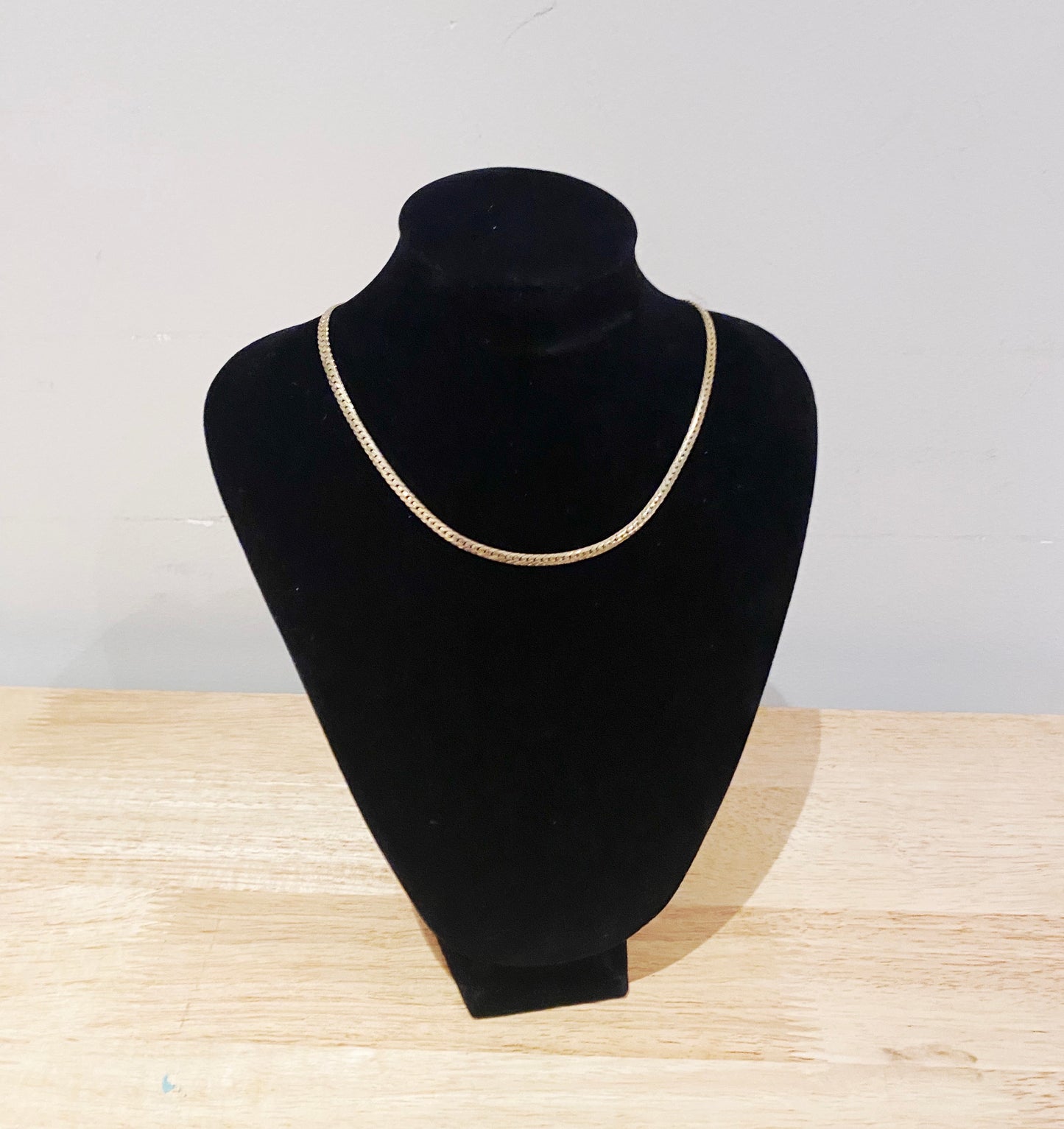 Gold necklace on a black mannequin bust against a light gray background