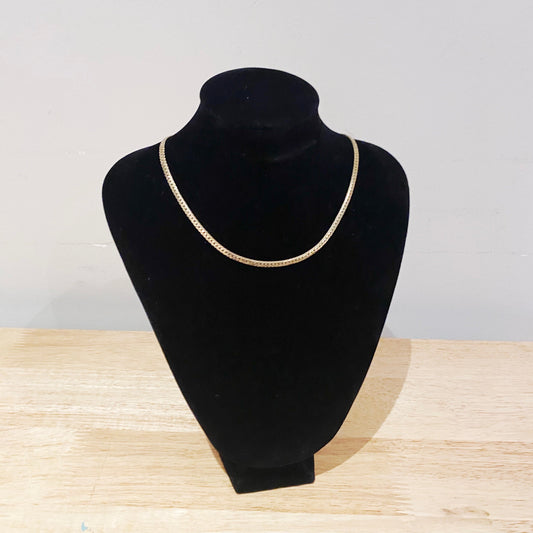 Gold necklace on a black mannequin bust against a light gray background