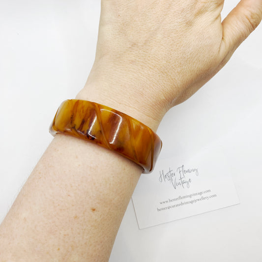 1940s carved Bakelite bangle in amber marbled tones worn on wrist