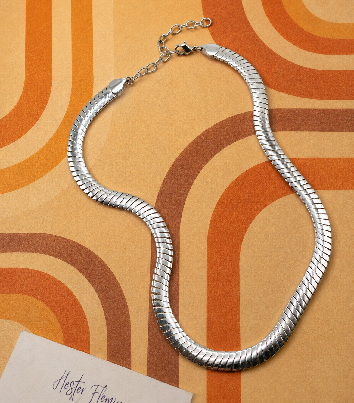Silvertone herringbone chain necklace, circa 1970s. Laid flat on 70s graphic background. 