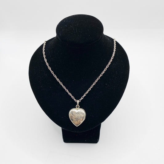 Circa 1980s sterling silver heart locket necklace shown closed on display bust.