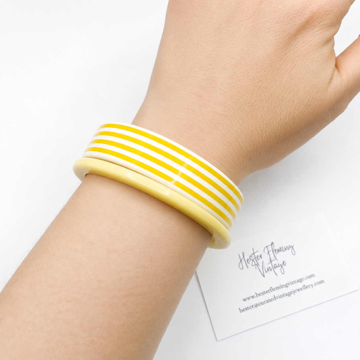 French yellow and white striped bangle set on a wrist with a white background. 