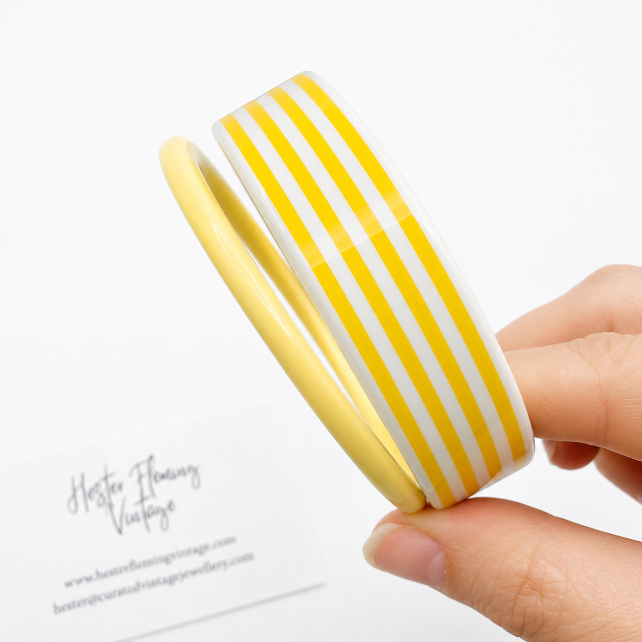Yellow and white striped bangle held by a hand on a white background
