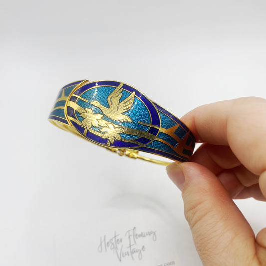 Close up of retro 80s cloisonne bangle, blue & green enamel. Gilt flying swan over palm trees.