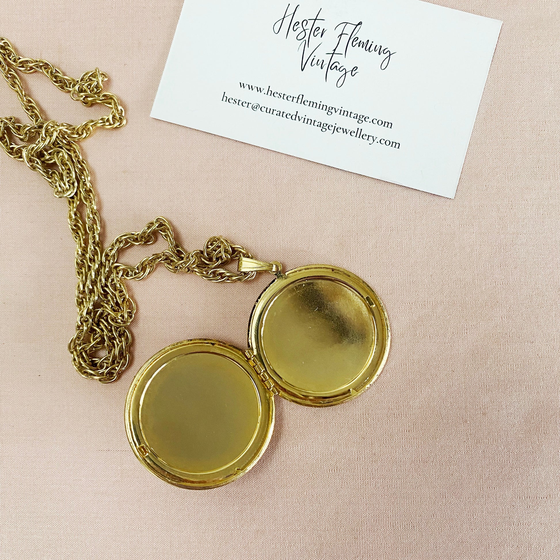 Open locket and chain on light pink background.