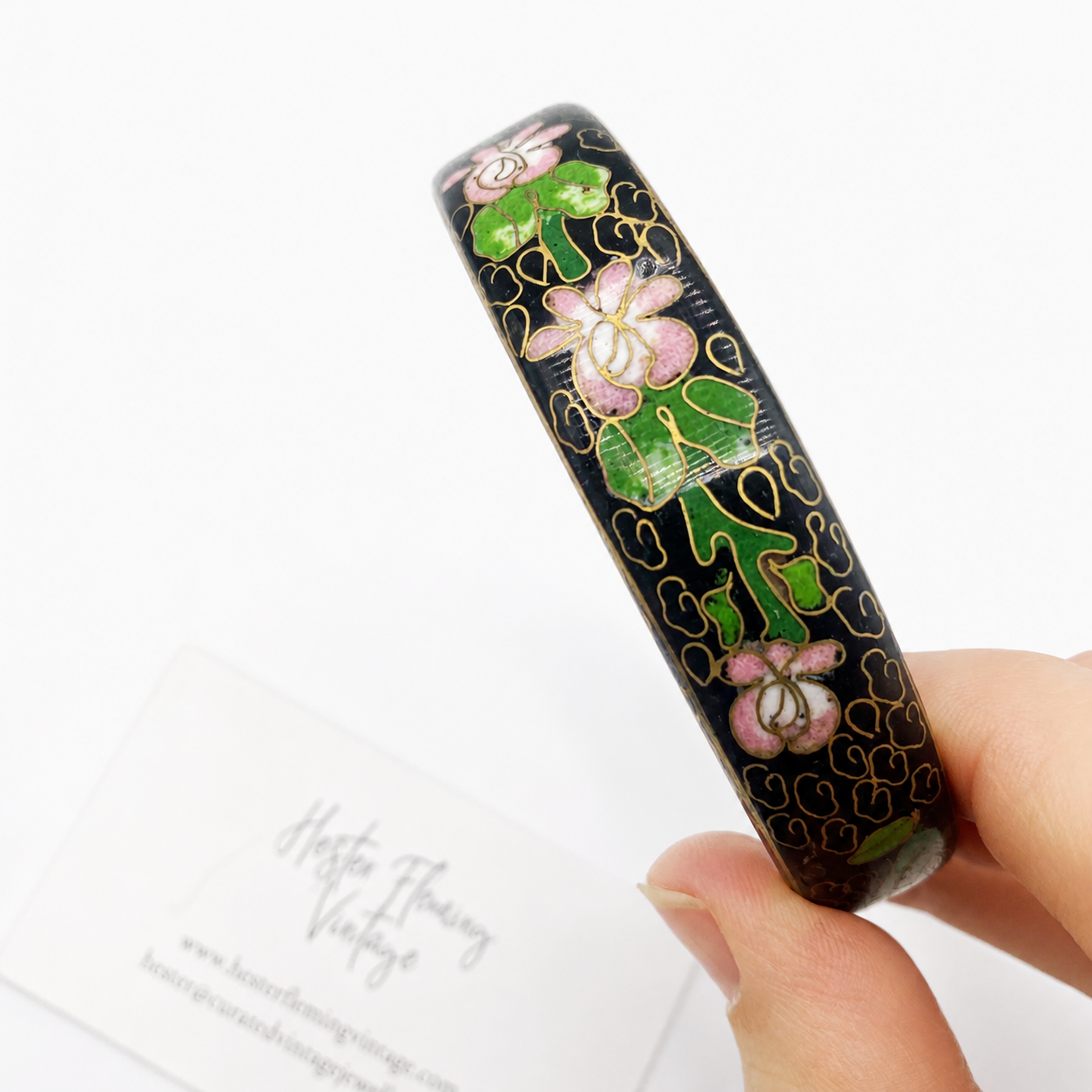 Vintage 70s Cloisonne' bangle with floral patterns held by a hand on a white background
