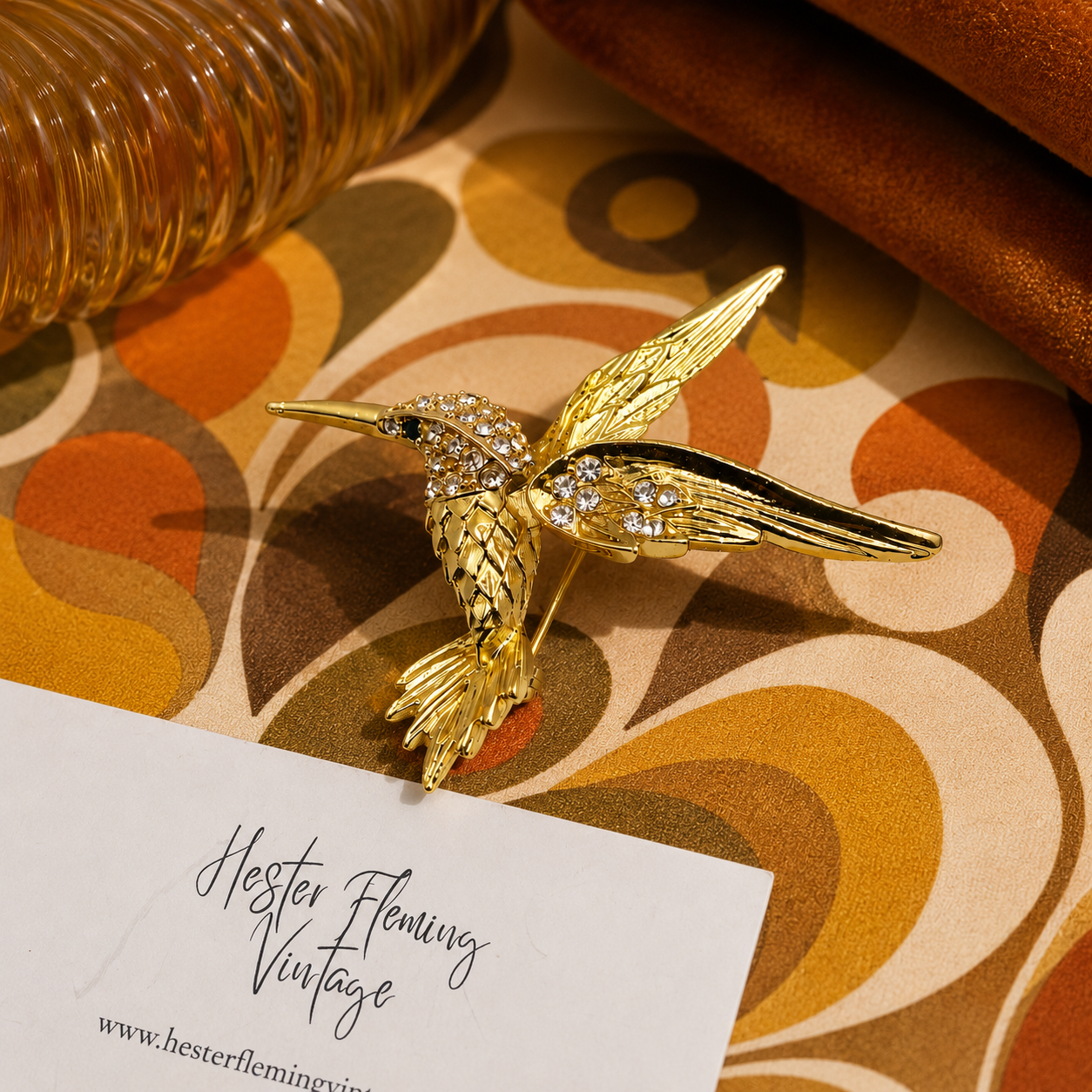 Gold hummingbird brooch on a patterned fabric with 'Hester Fleming Vintage' card.
