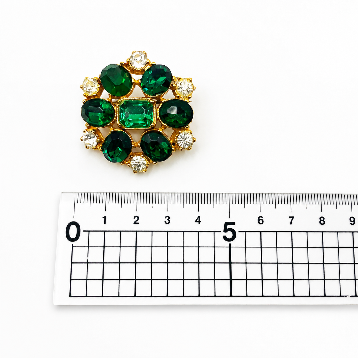 Vintage emerald crystal brooch, placed next to a ruler for size. 