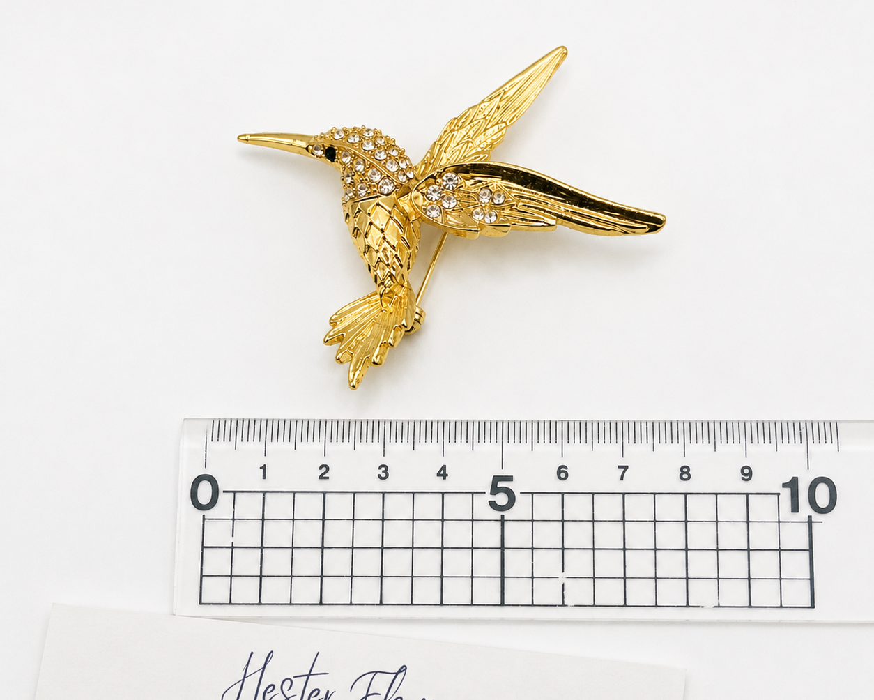 90s Hummingbird brooch, placed next to a ruler for size. 