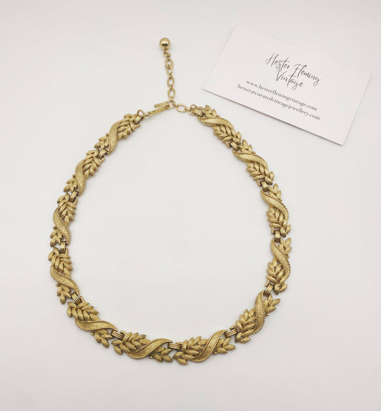 Flat lay of vintage Crown Trifari gold-tone necklace, collectible mid-century jewellery.
