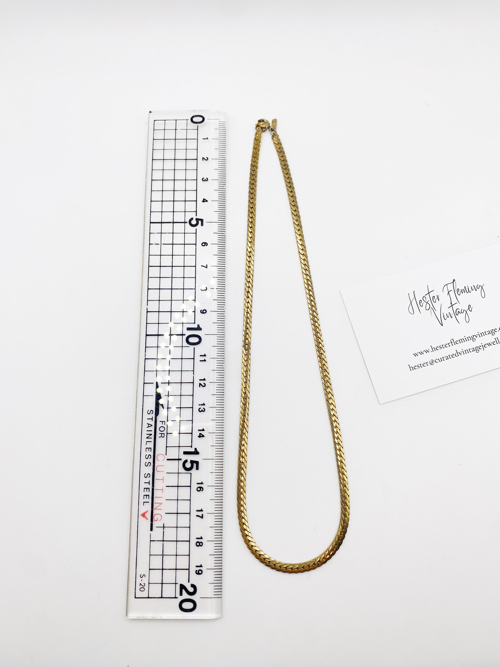 Gold chain necklace next to a ruler on a white background