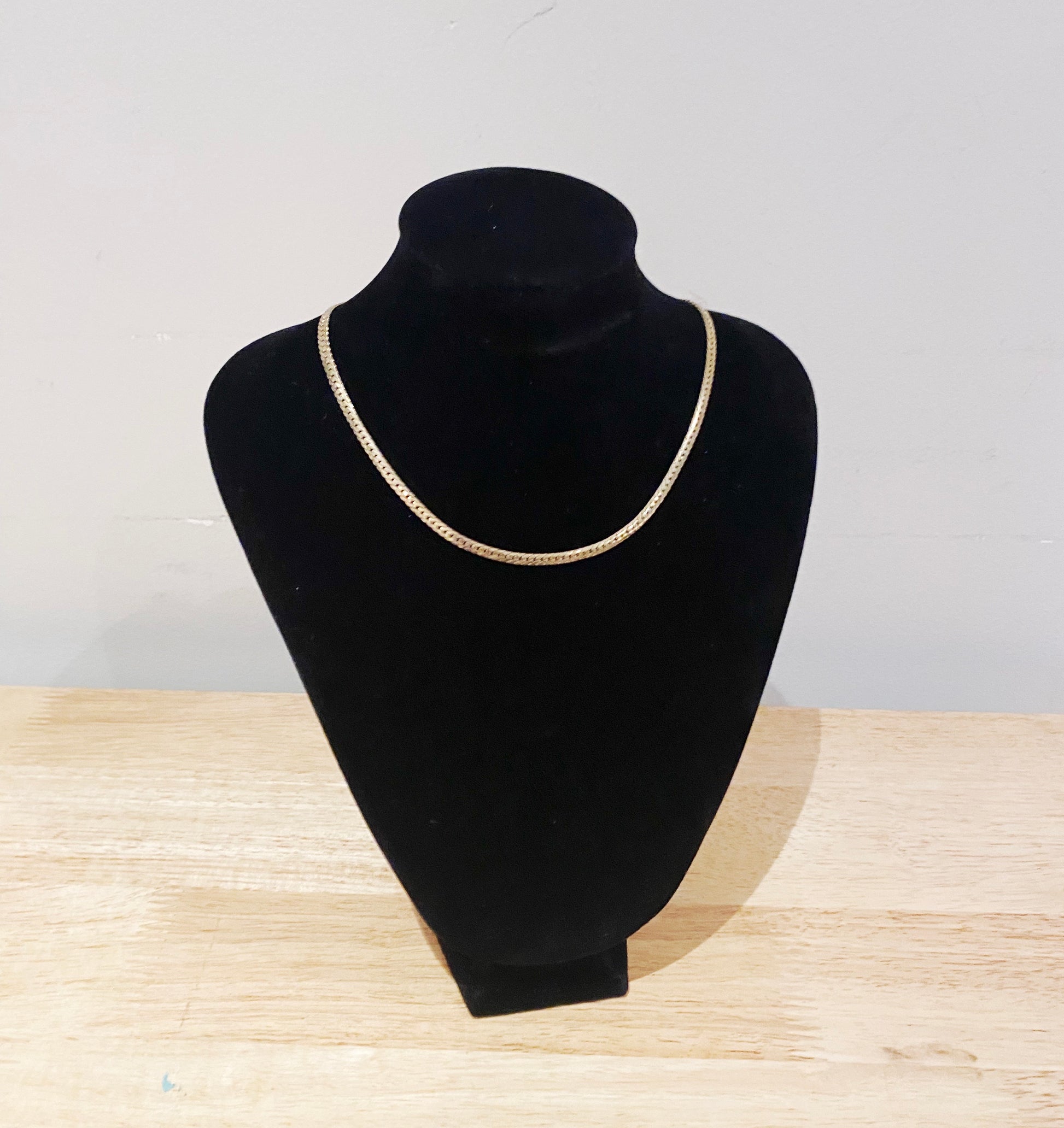 Gold necklace on a black mannequin bust against a light gray background