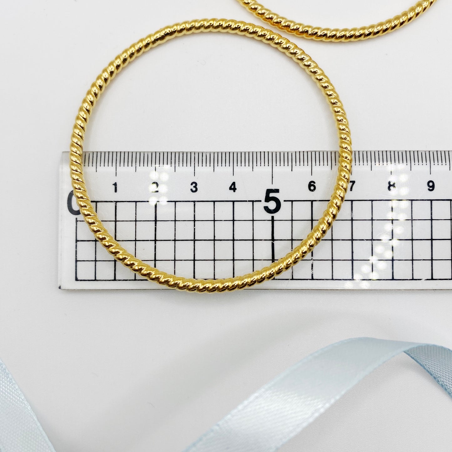 Close-up of vintage gold-plated bangles with textured finish, 1980s costume jewellery, next to ruler.
