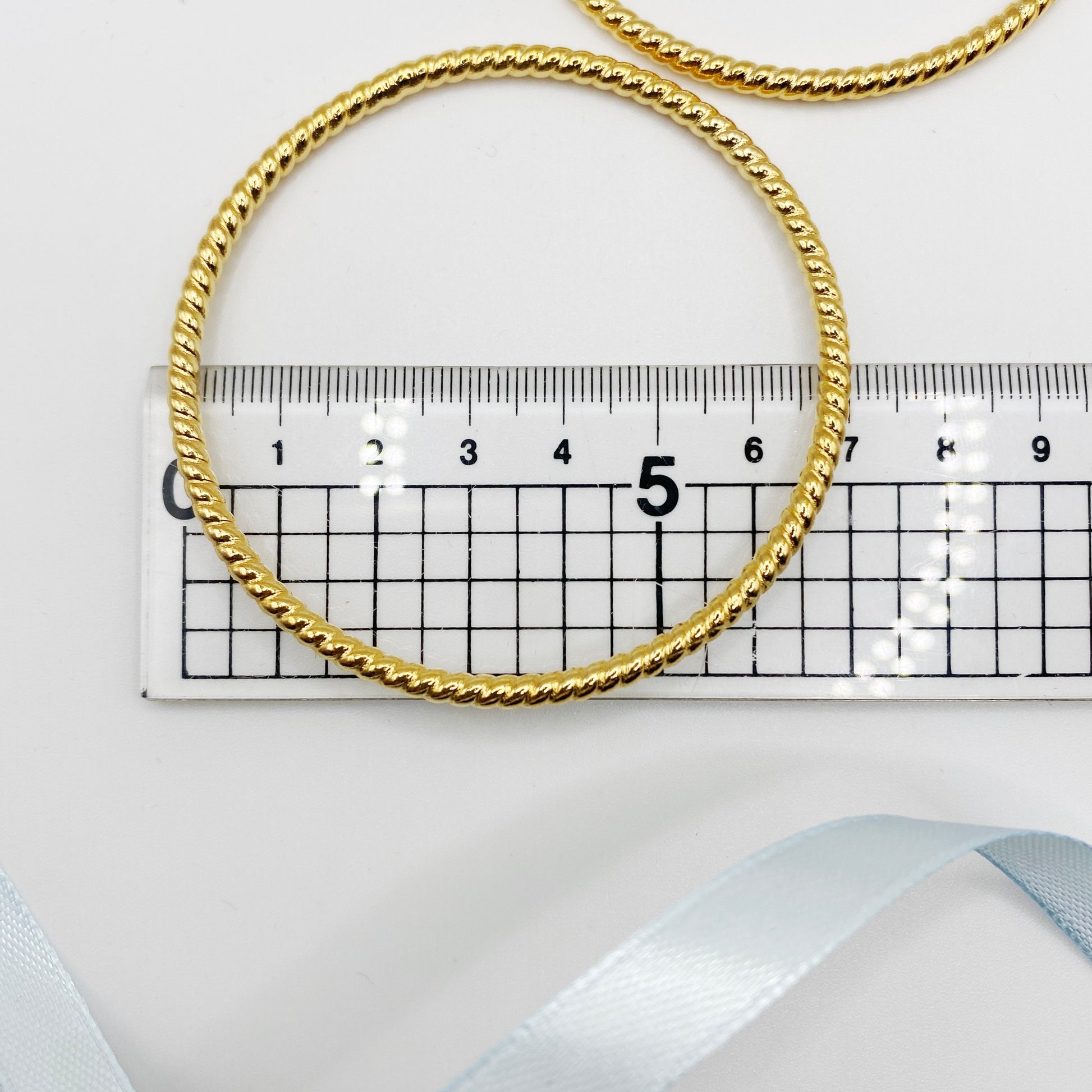 Close-up of vintage gold-plated bangles with textured finish, 1980s costume jewellery, next to ruler.