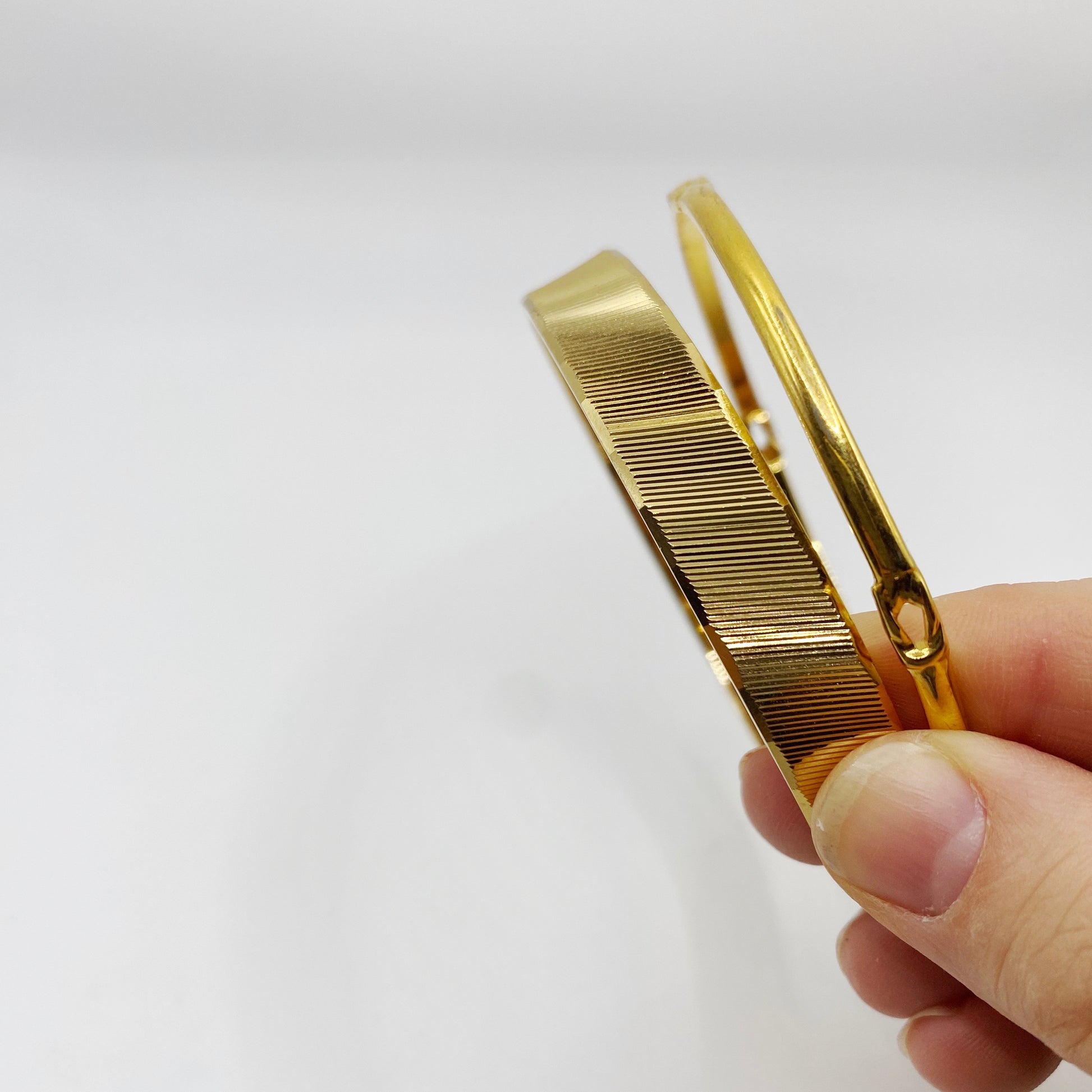 Stacked 1970s Monet gold bangles, one slim and one wide, collectible vintage designer jewellery.